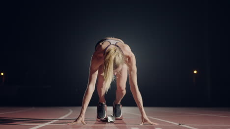 One-woman-in-the-dark-at-the-stadium-is-preparing-to-start-a-race-on-the-track.-Slow-motion-woman-starts-from-hunger-strikes-in-the-stadium-in-the-dark